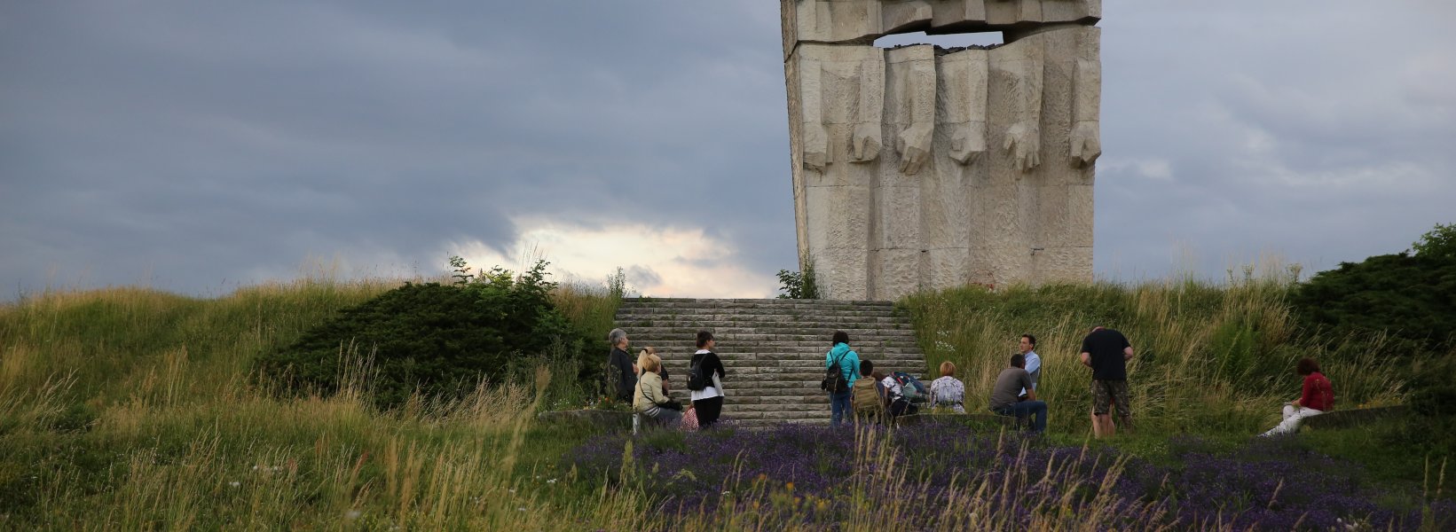 Współczesna fotografia. Miejsce pamięci KL Plaszow. Grupa ludzi stojąca przed Pomnikiem Ofiar Faszyzmu.
