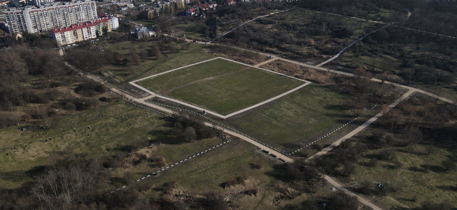 Zdjęcie współczesne, kolorowe, wykonane z drona. Na zdjęciu widok Pomnika Ofiar Faszyzmu oraz rozległego terenu byłego obozu Plaszow.